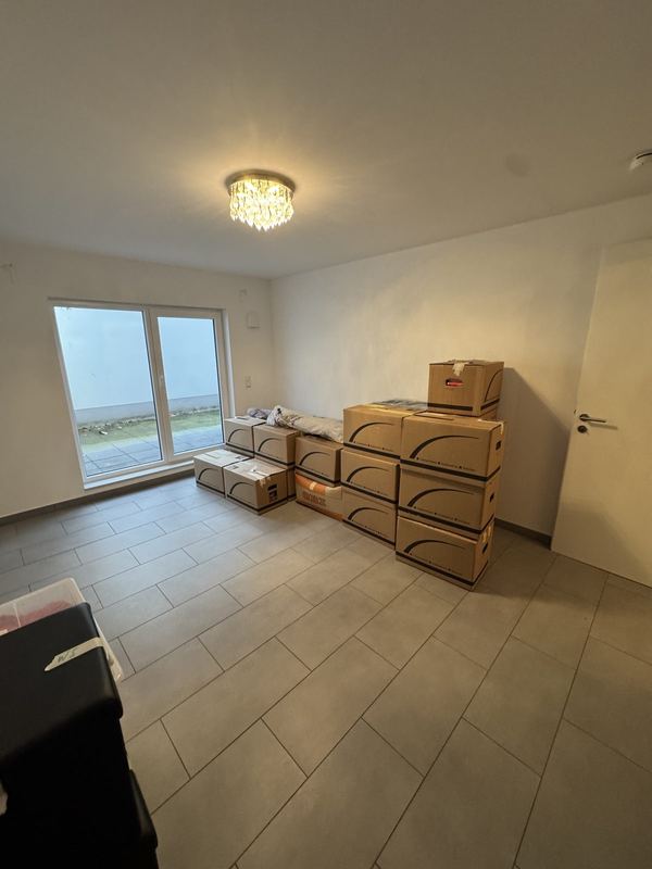Kartonstapel in einem noch leeren Neubauzimmer, dahinter ein bodentiefes Fenster