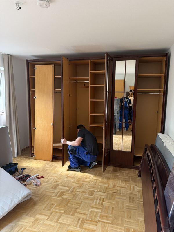 Mitarbeiter justiert im Schlafzimmer die Türen eines Kleiderschranks mit mehreren Türen
