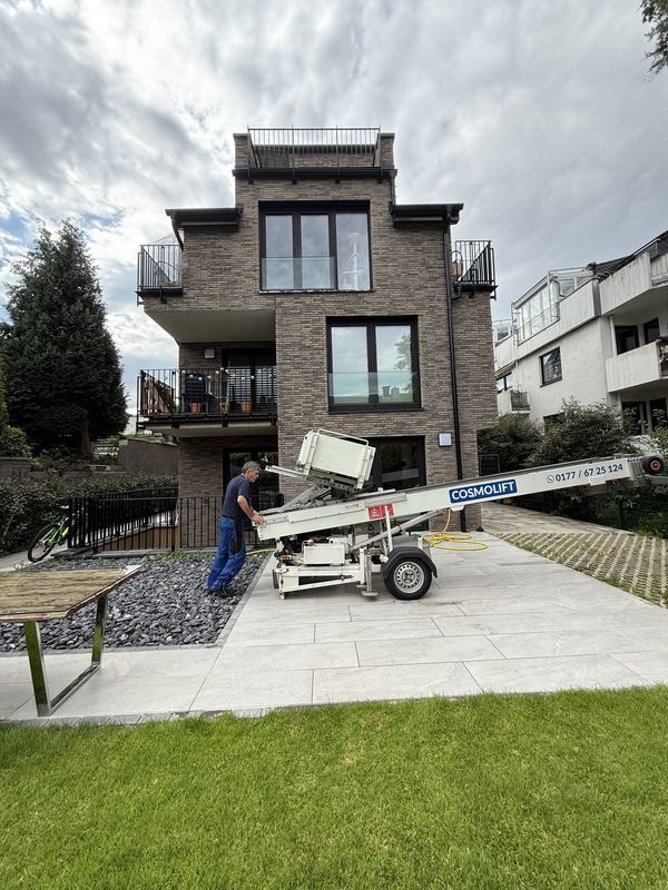 Mitarbeiter stellt einen Möbellift auf der Einfahrt vor einem Wohnhaus auf