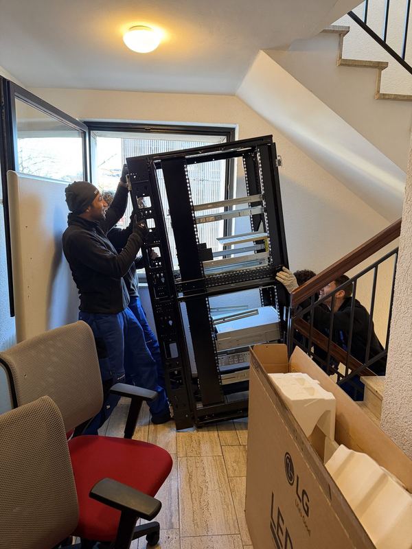 Drei Kollegen tragen einen offenen Serverschrank ein Treppenhaus hinunter