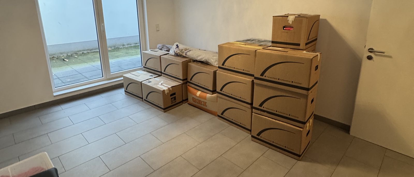 Privatumzug in Leverkusen: gestapelte Umzugskartons in einem hellen Zimmer mit Fliesenboden und Terrassentür