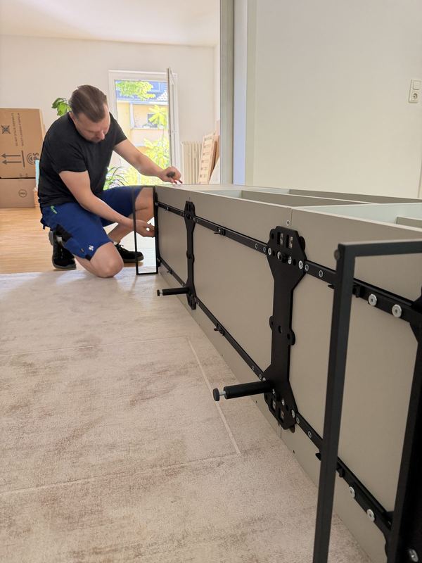 Ein Sideboard liegt am Boden, davor kniend bringt ein Mitarbeiter die Beschläge an
