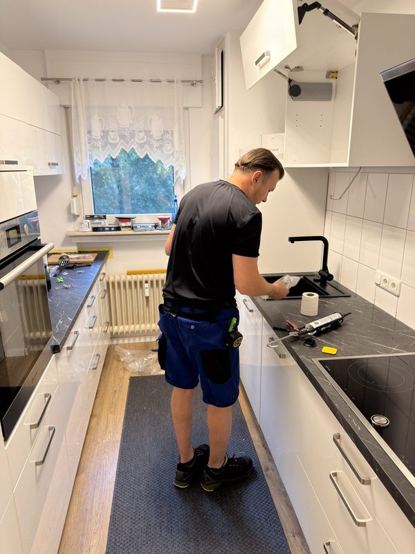 Ein Mitarbeiter senkt eine schwarze Spüle in den fertig ausgesägten Ausschnitt der Arbeitsplatte.