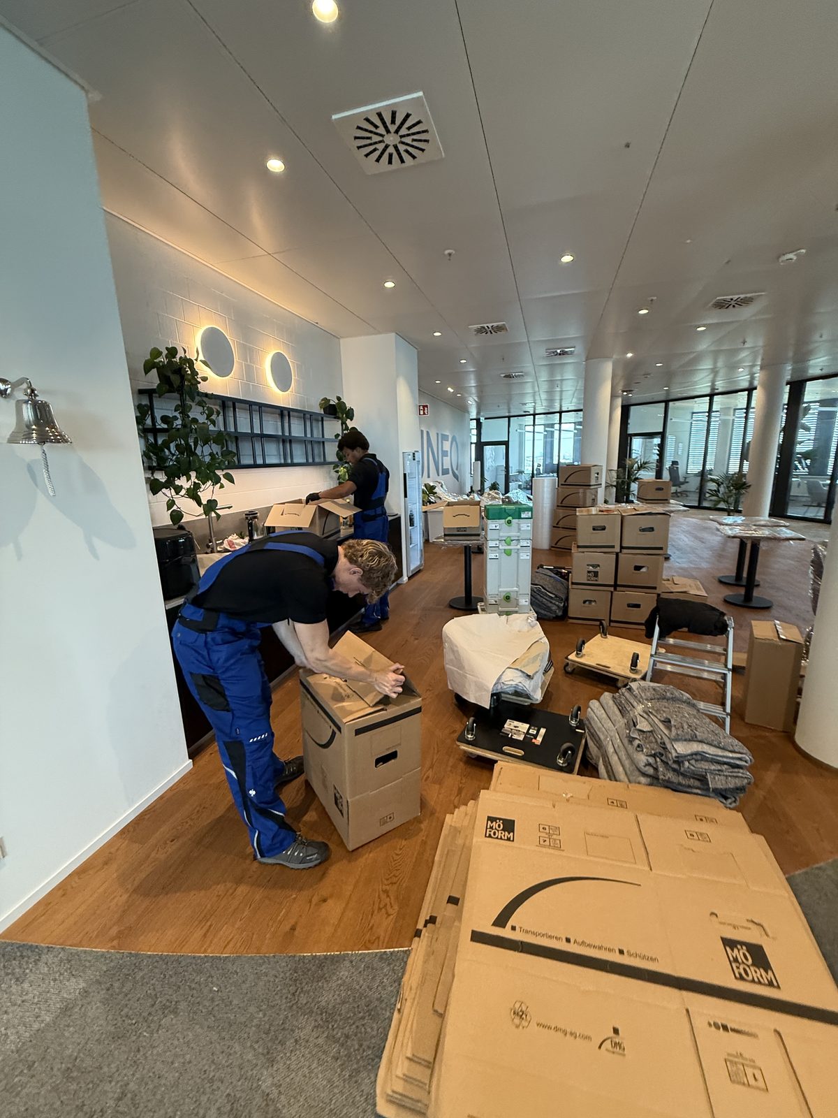 Ein Mitarbeiter klebt einen Umzugskarton zu, im Hintergrund stapeln sich bereits fertig gepackte Kartons im Büro.