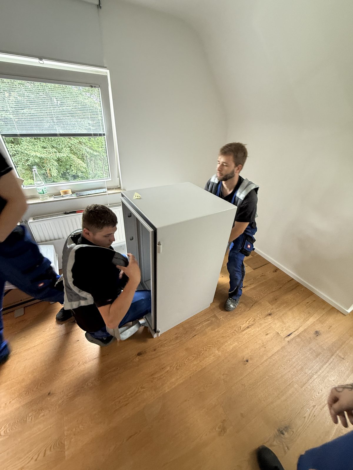 Zwei Mitarbeiter tragen ein weißes Einbaugerät gemeinsam durch einen leeren Raum.