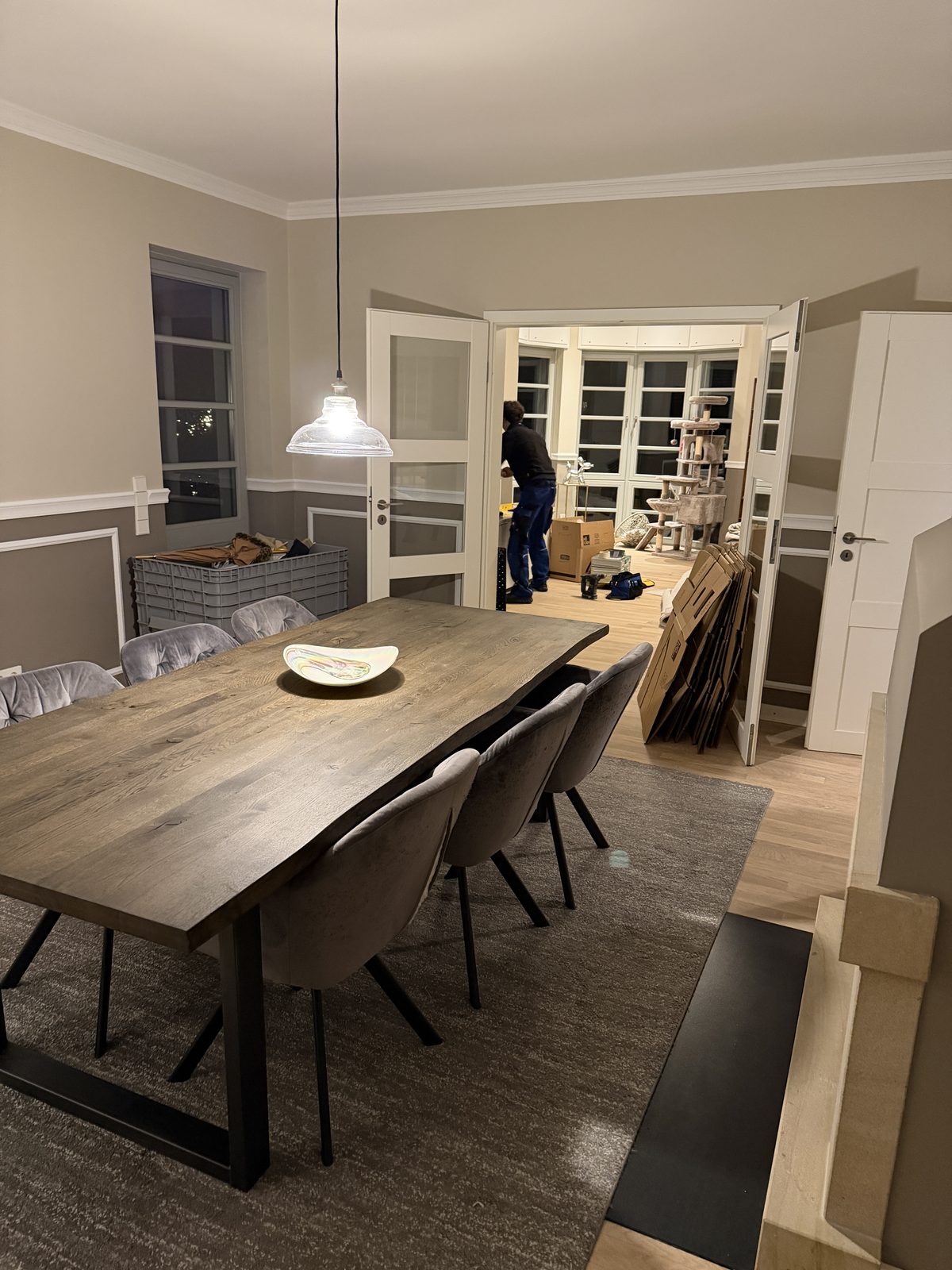 Ein fertig eingerichtetes Esszimmer mit gedecktem Tisch, im Nebenraum werden die leeren Kartons zusammengelegt.