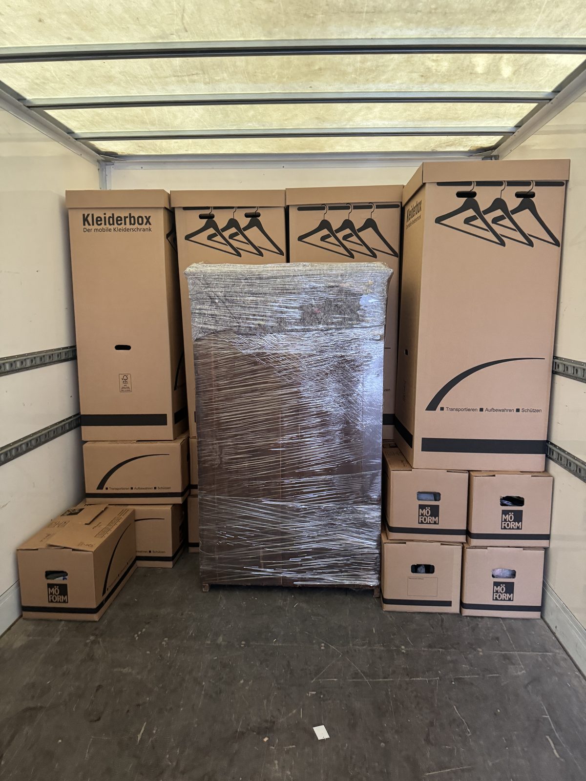 Im Laderaum des Umzugswagens stehen mehrere Kleiderboxen in einer Reihe, dazwischen ein folierter Schrank.