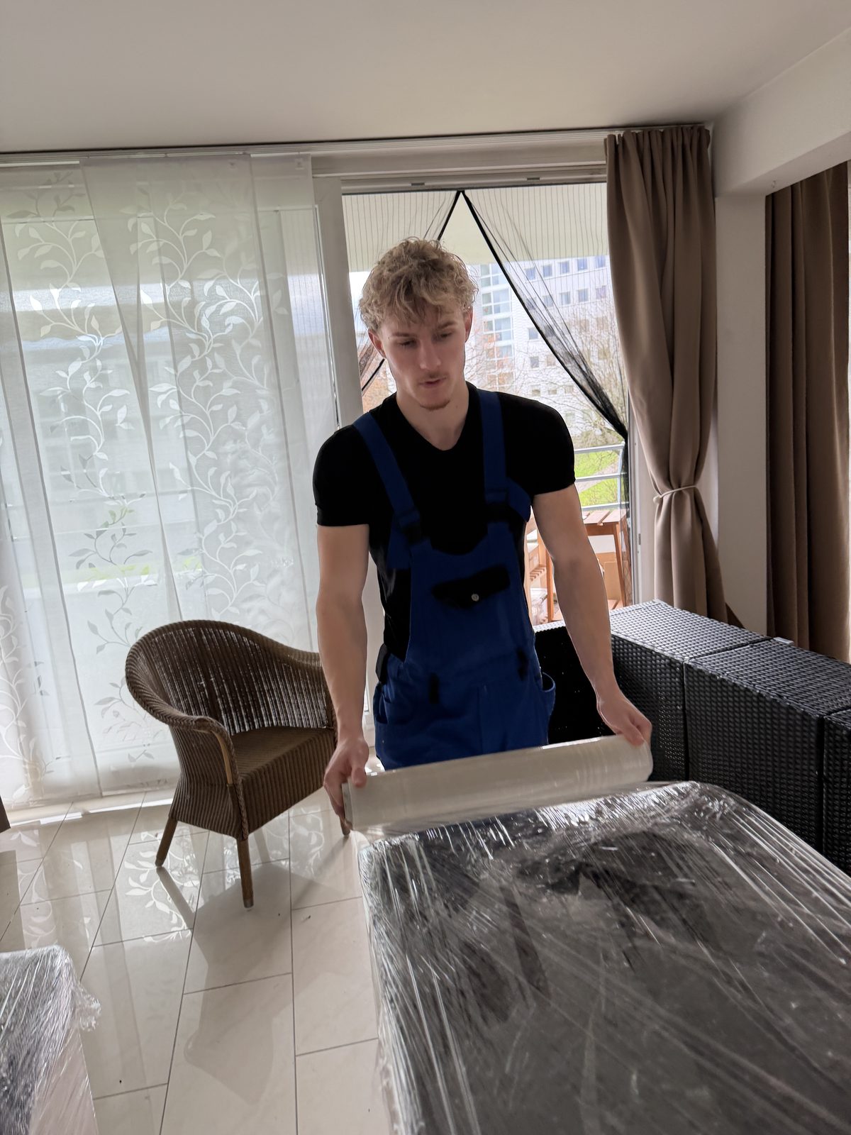 Ein Mitarbeiter zieht in der Wohnung Stretchfolie um ein Möbelstück, damit es beim Transport geschützt ist.