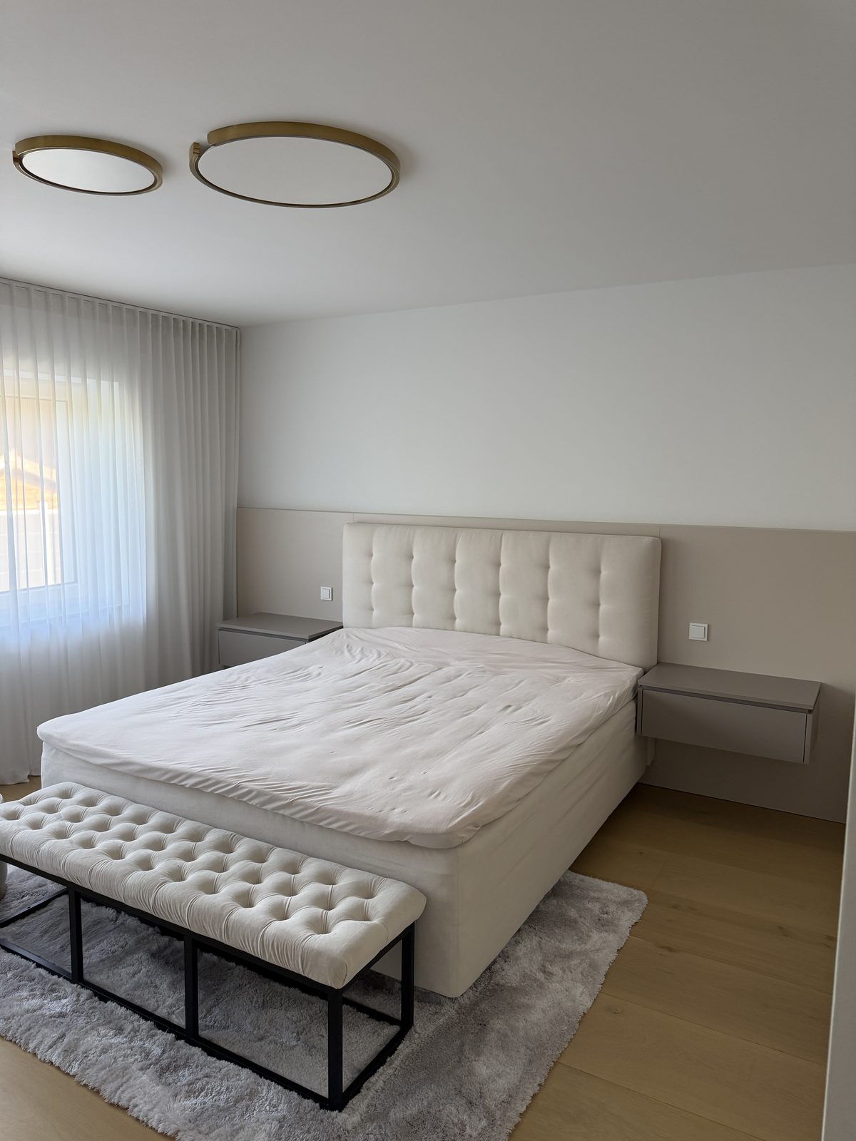 Ein helles Schlafzimmer mit aufgebautem Boxspringbett, am Fußende steht eine Bank.