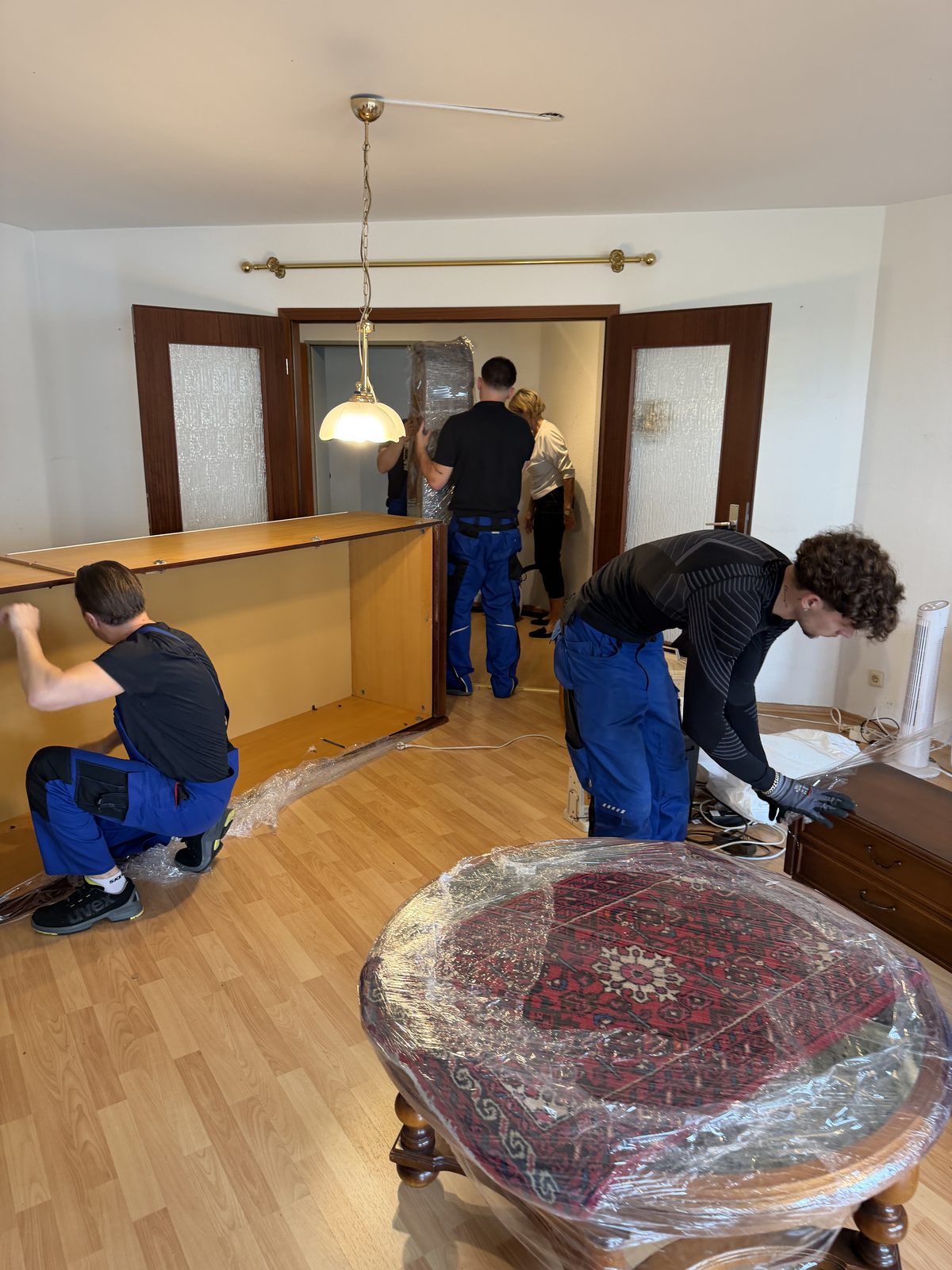 Vier Mitarbeiter bauen im Wohnzimmer den Korpus einer breiten Schrankwand zusammen.