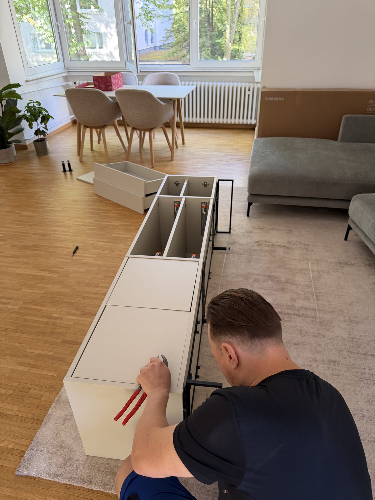 Von oben gesehen: Ein Mitarbeiter befestigt die Auszüge an einem auf dem Boden liegenden Sideboard.