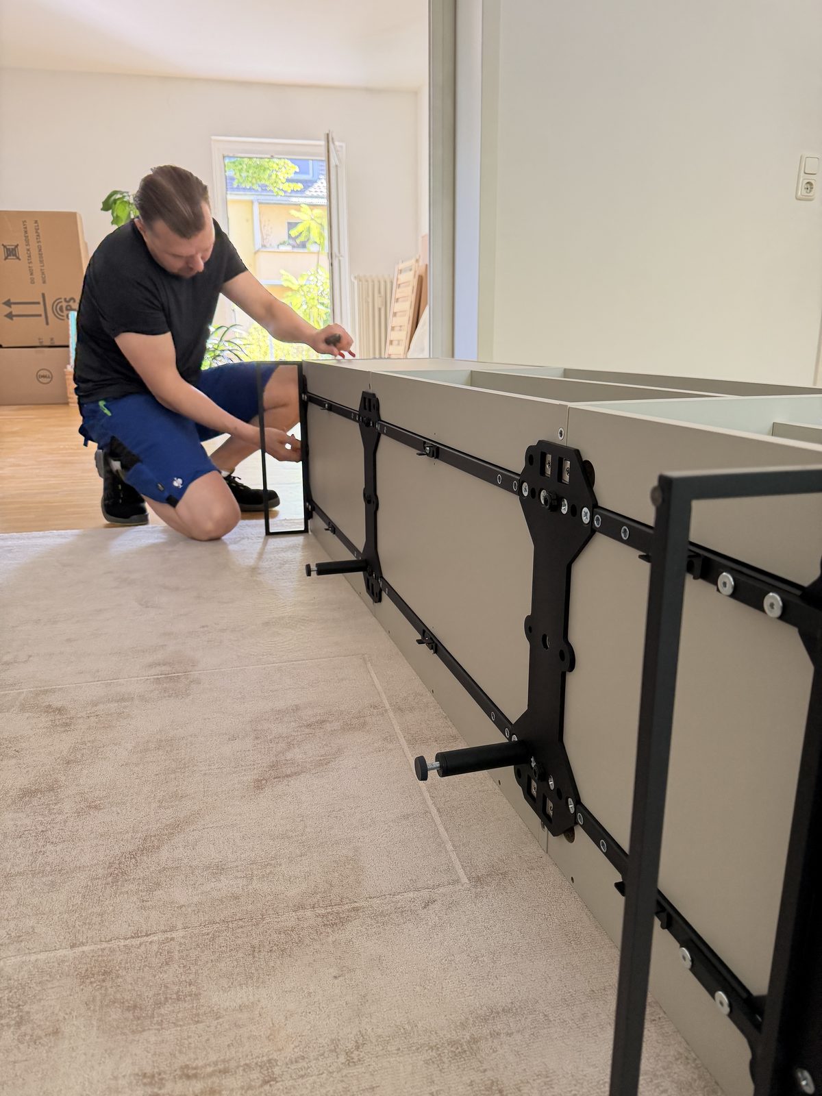 Ein Mitarbeiter kniet vor einem liegenden Sideboard und bringt die Beschläge an.