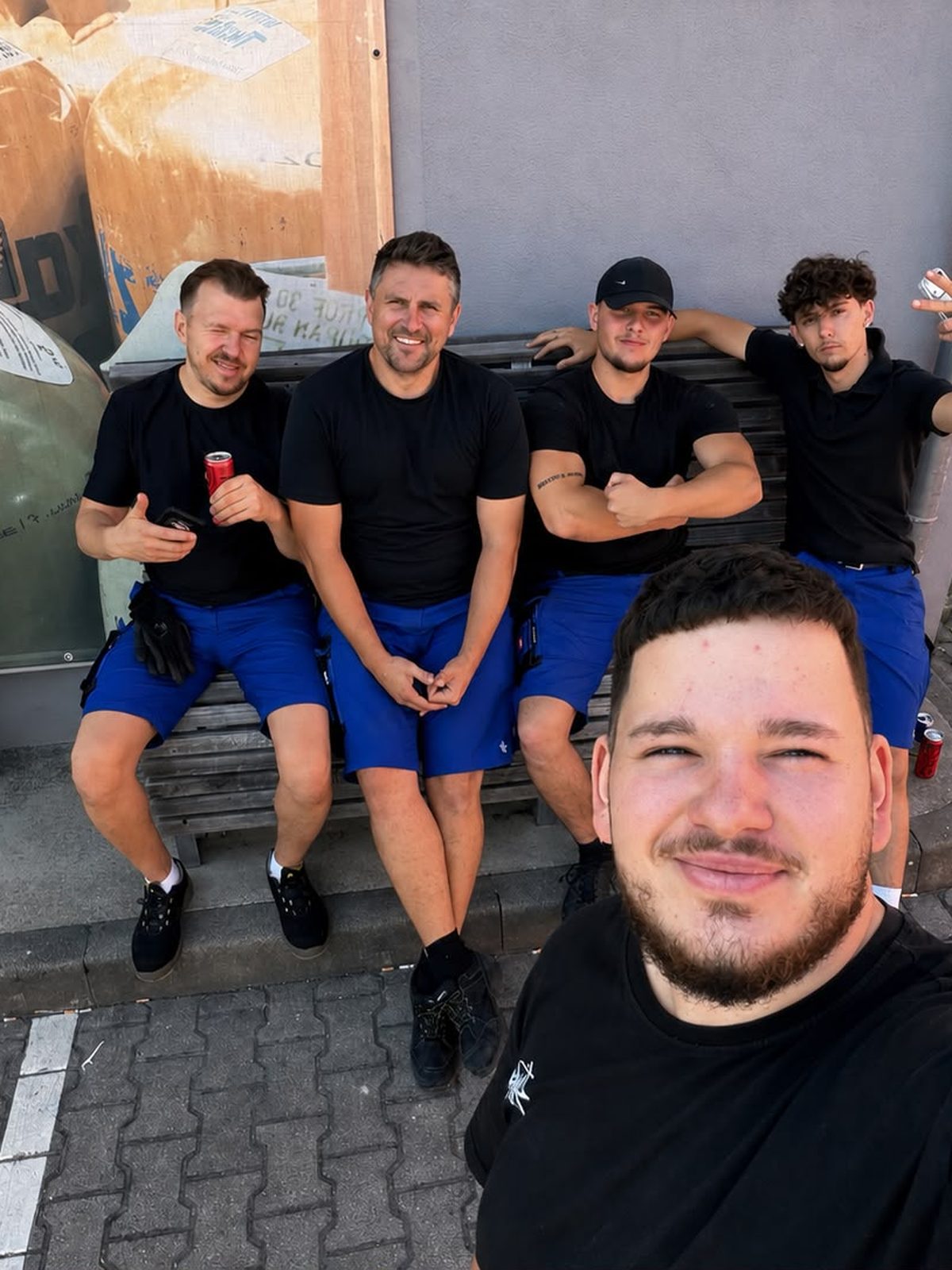 Fünf Mitarbeiter in Arbeitskleidung sitzen in der Sonne nebeneinander auf einer Bank.