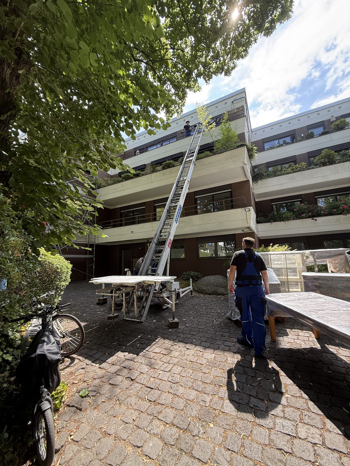 Ein Möbellift steht ausgefahren an einem Wohnhaus mit mehreren Etagen, unten wartet ein Mitarbeiter auf die Ladung.